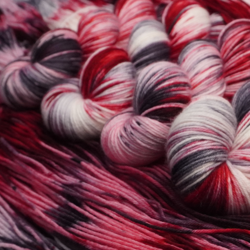 Close-up of multicolored yarn skeins with red, pink, and black patterns.
