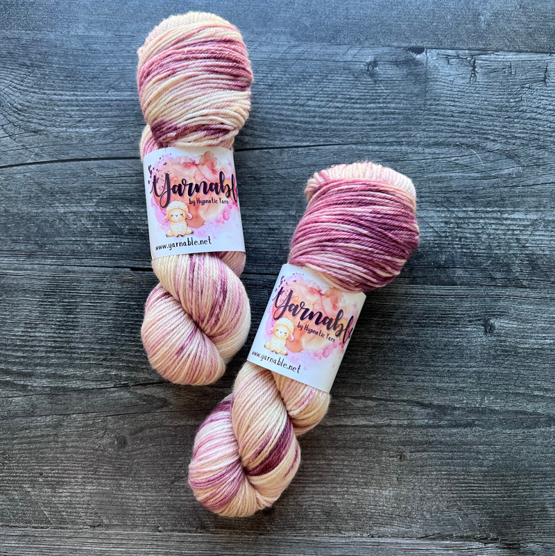 Hand-dyed yarn skeins in soft cream, blush pink, and mauve tones, twisted and arranged side by side with subtle variegation.
