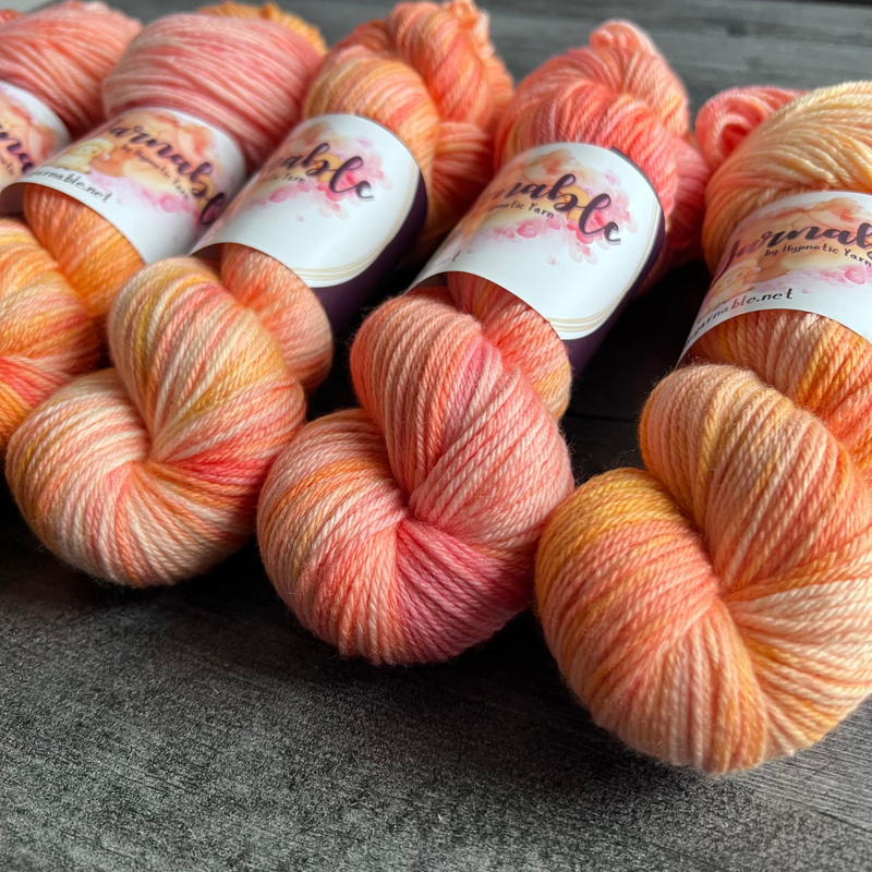Multiple hand-dyed yarn skeins in warm pink, peach, and creamy yellow shades, displayed side by side with Yarnable by Hypnotic Yarn branding visible.