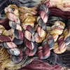 Close-up of multiple twisted skeins of hand-dyed yarn featuring burgundy, charcoal gray, ivory, and mustard color variations.