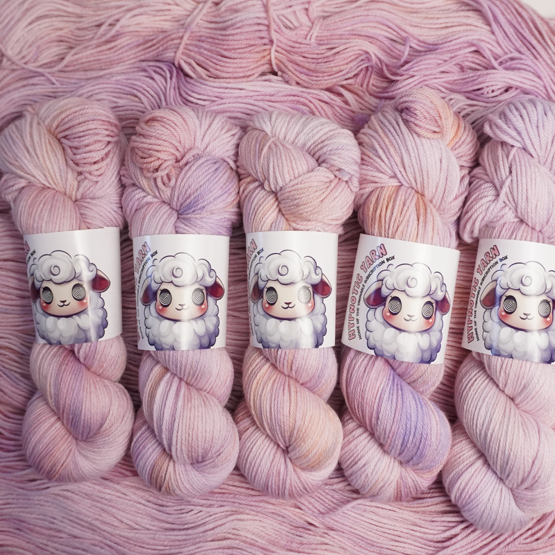 Hand-dyed yarn skeins in soft pastel pink with subtle lavender and cream variations, shown twisted and arranged side by side.