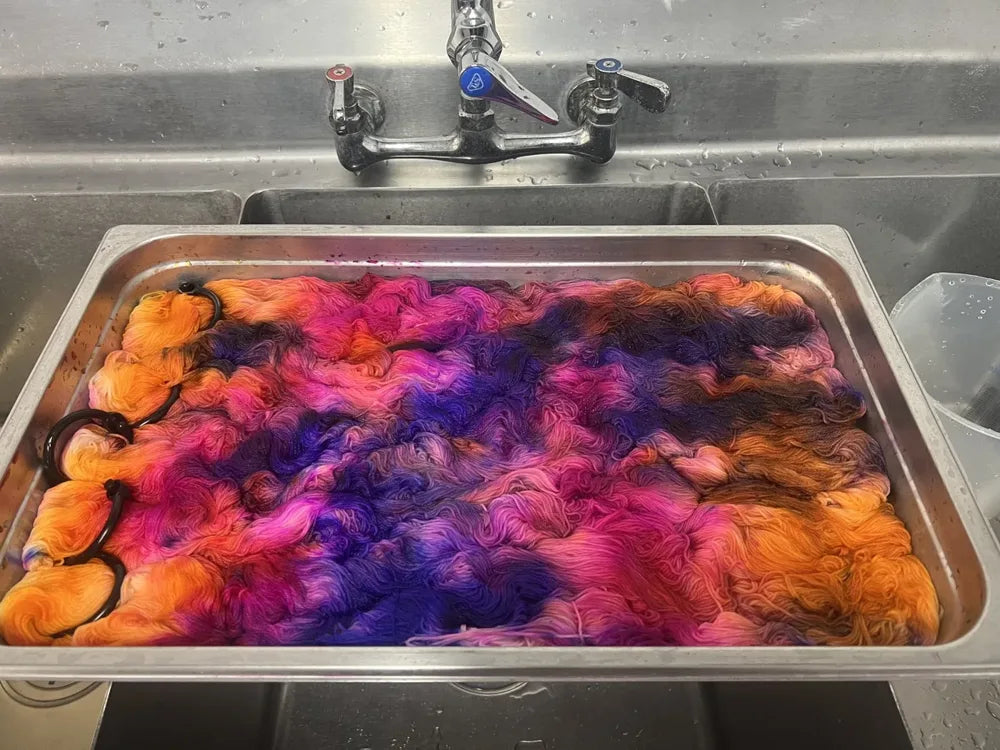 A steel dye pot full of skeins soaking in orange, hot pink and purple dye