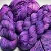 Bright purple speckled Zodiac Sagittarius yarn skeins and a yarn cake piled on purple knit swatches