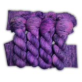 Four bright purple Zodiac Sagittarius yarn skeins with dark speckles laid over a knit swatch