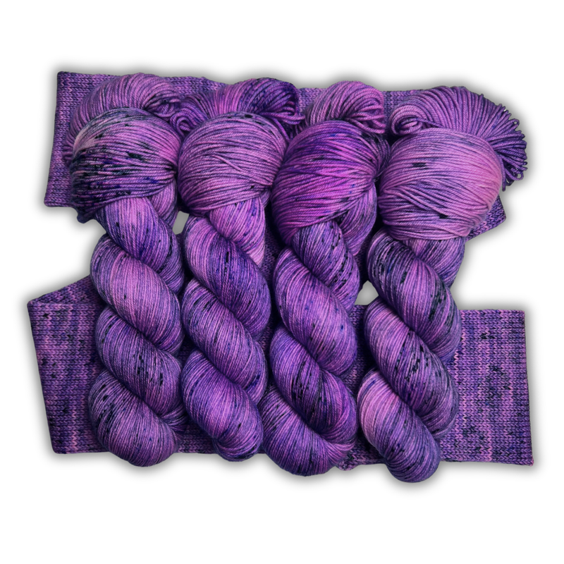 Four bright purple Zodiac Sagittarius yarn skeins with dark speckles laid over a knit swatch