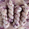 Hand-dyed yarn skeins in soft cream, blush pink, and mauve tones, twisted and arranged side by side with subtle variegation.