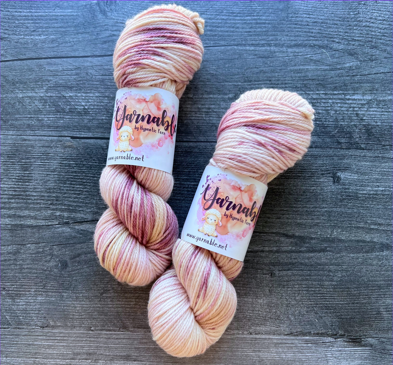 Hand-dyed yarn skeins in soft cream, blush pink, and mauve tones, twisted and arranged side by side with subtle variegation.