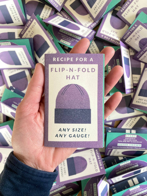 Flip-N-Fold Hat mini zine held in hand, printed with Recipe for a Flip-N-Fold Hat