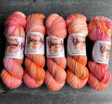Multiple hand-dyed yarn skeins in warm pink, peach, and creamy yellow shades, displayed side by side with Yarnable by Hypnotic Yarn branding visible.