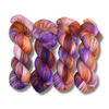Four multicolored hand-dyed yarn skeins in warm orange and yellow with purple accents, photographed on a textured backdrop made of coordinating yarn.