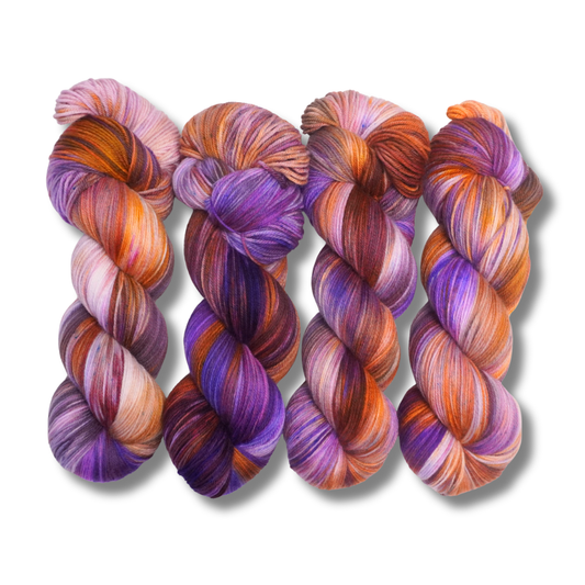 Four multicolored hand-dyed yarn skeins in warm orange and yellow with purple accents, photographed on a textured backdrop made of coordinating yarn.