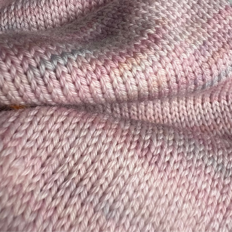 Hand-dyed yarn skeins in soft pastel pink with subtle lavender and cream variations, shown twisted and arranged side by side.