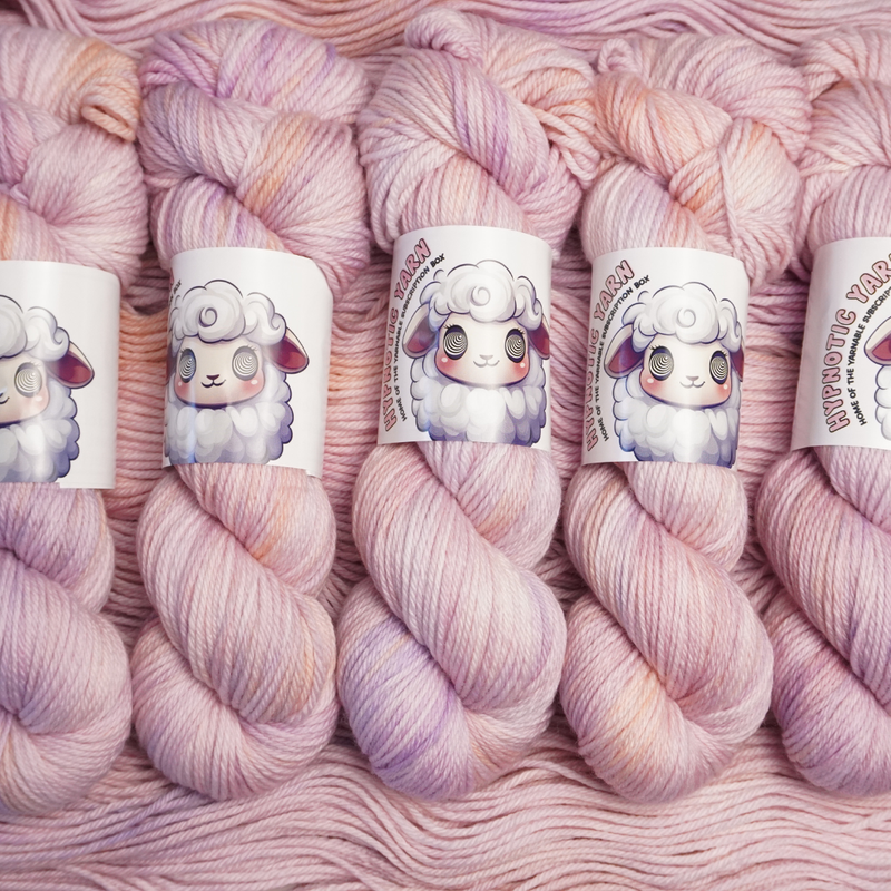 Hand-dyed yarn skeins in soft pastel pink with subtle lavender and cream variations, shown twisted and arranged side by side.