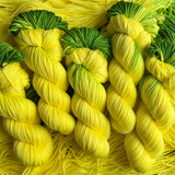 Hand-dyed yarn skeins in bright yellow with green accents, twisted and arranged on a matching yellow yarn background.