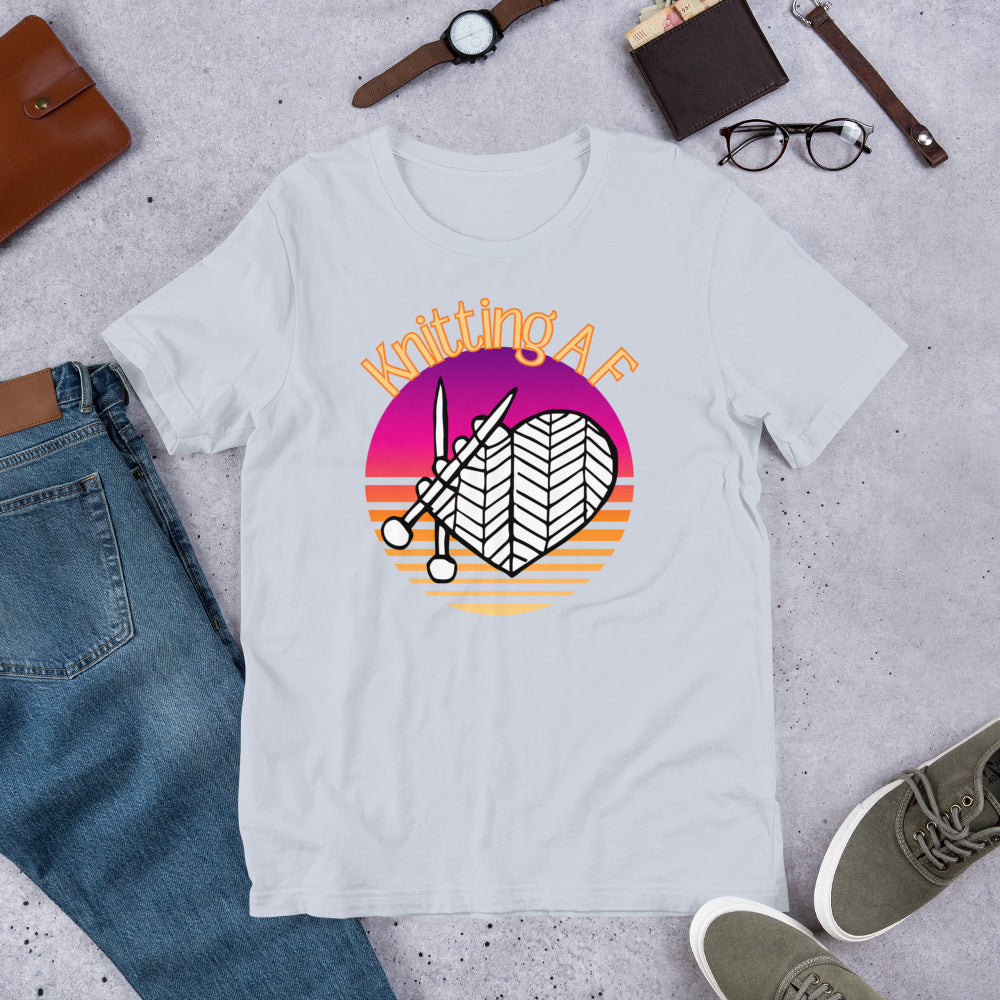 Light blue scoop neck tee with the Knitting AF design in magenta and orange sunset stripes with knitting needles