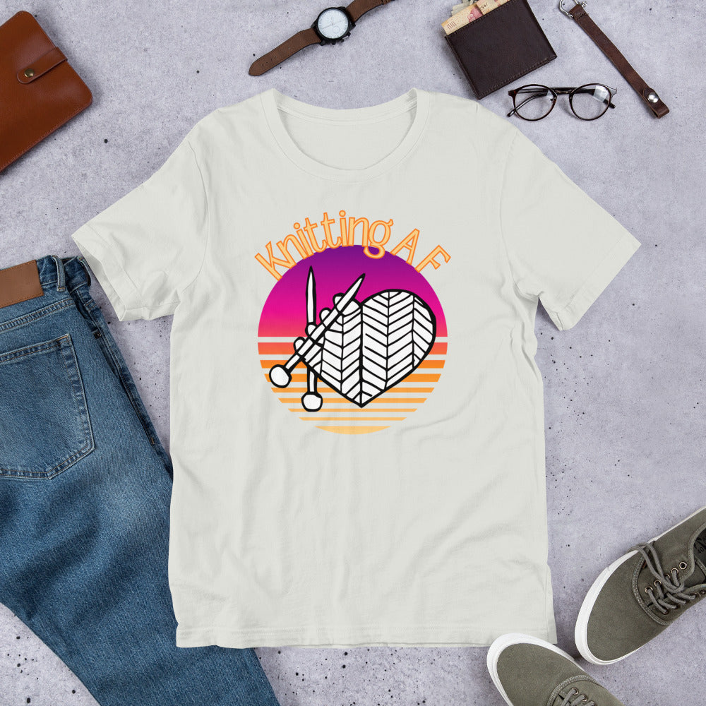 Silver scoop neck tee with the Knitting AF design in magenta and orange sunset stripes with knitting needles