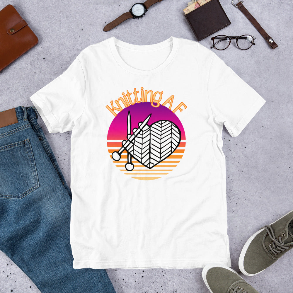 White scoop neck tee with the Knitting AF design in magenta and orange sunset stripes with knitting needles