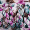 Twisted skeins of hand-dyed yarn with multicolored streaks of teal, pink, brown, and green on a light base, displayed on loose yarn.