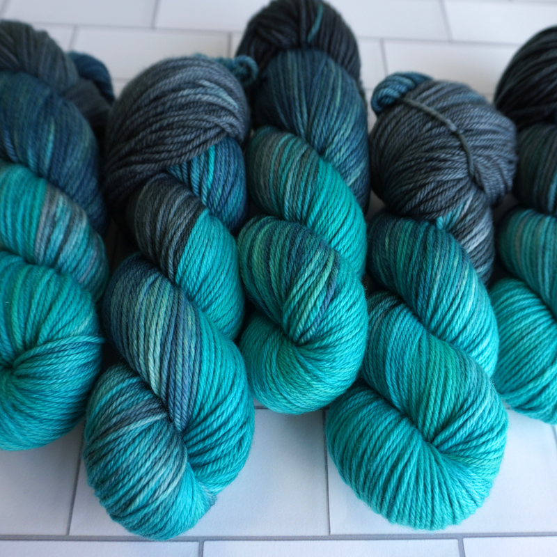 Multiple twisted skeins of hand-dyed yarn featuring gradients of aqua, teal, and slate gray.