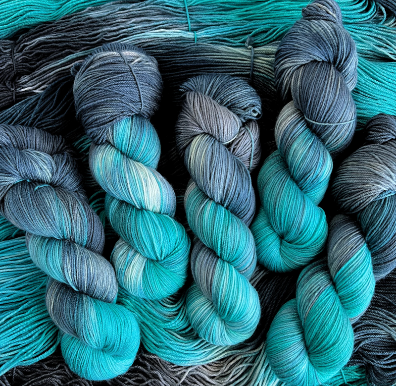 Multiple twisted skeins of hand-dyed yarn featuring gradients of aqua, teal, and slate gray.