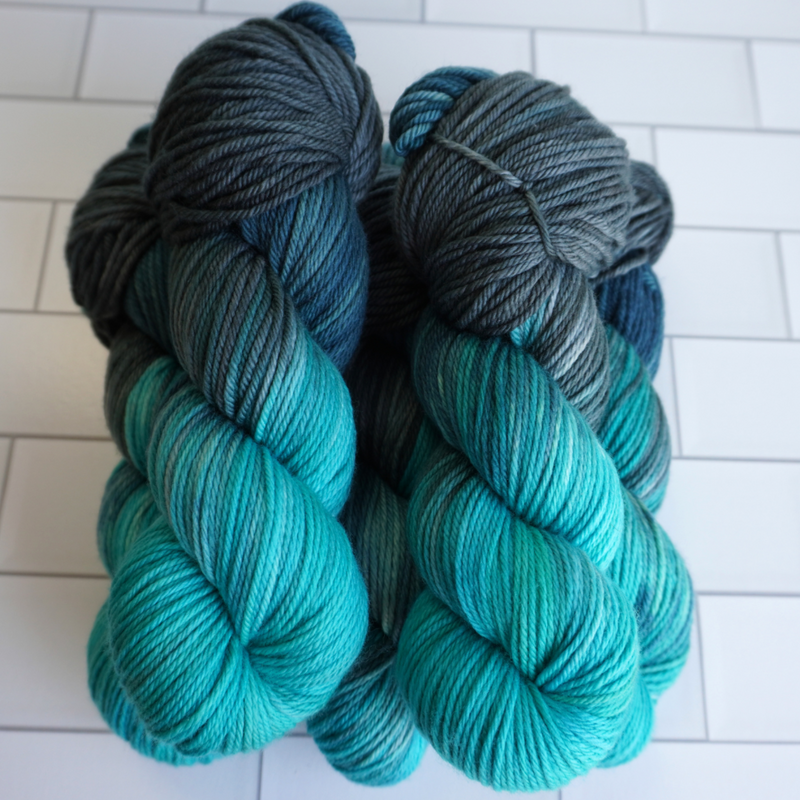 Multiple twisted skeins of hand-dyed yarn featuring gradients of aqua, teal, and slate gray.